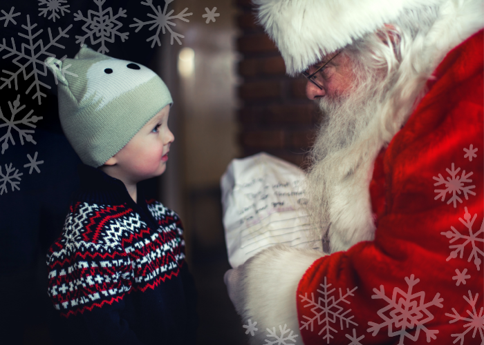 A young boy in winter clothing looks up at Santa Claus, who holds a letter in his hands.